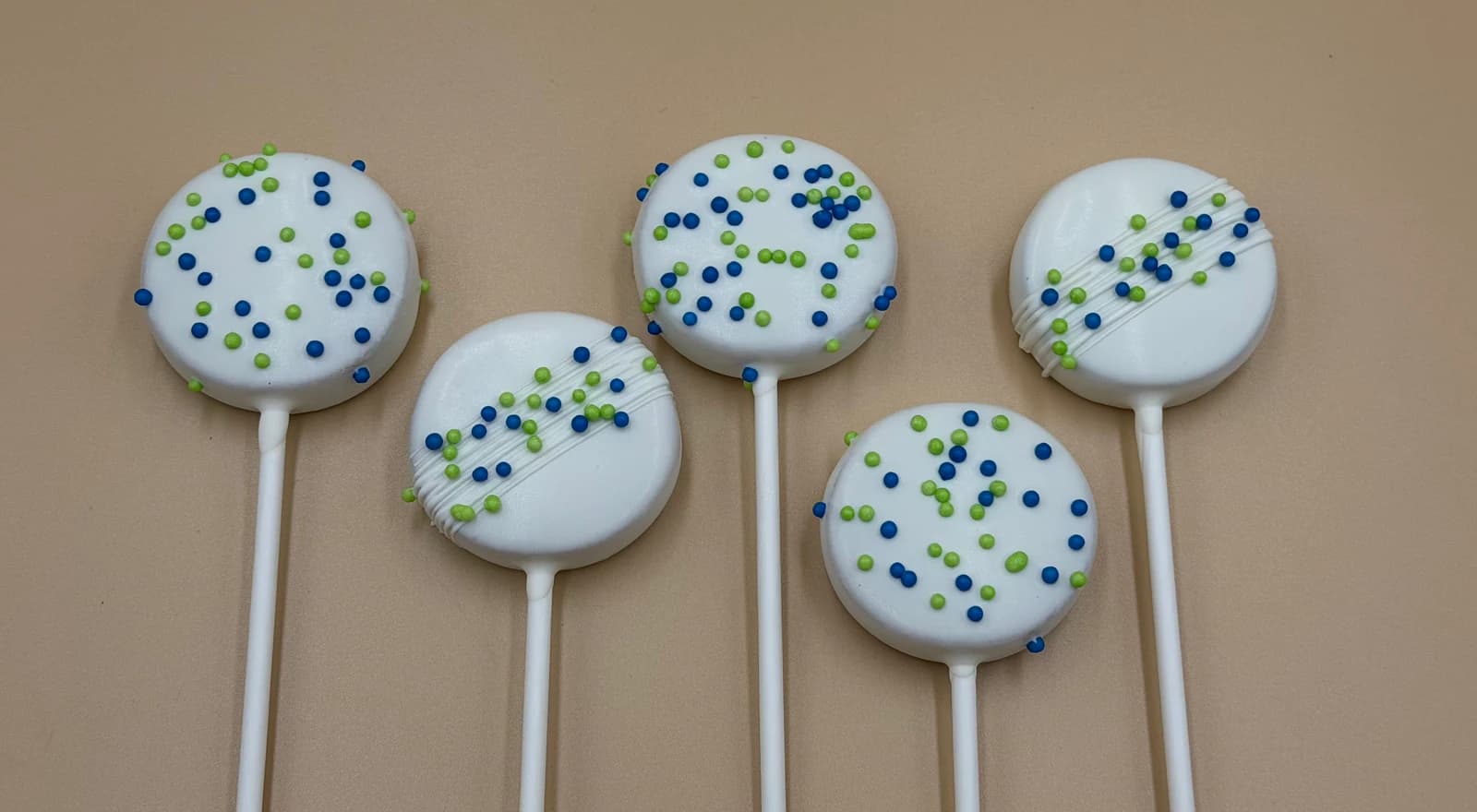 Classic white chocolate cake pops with diagonal drizzle and blue and green sprinkles