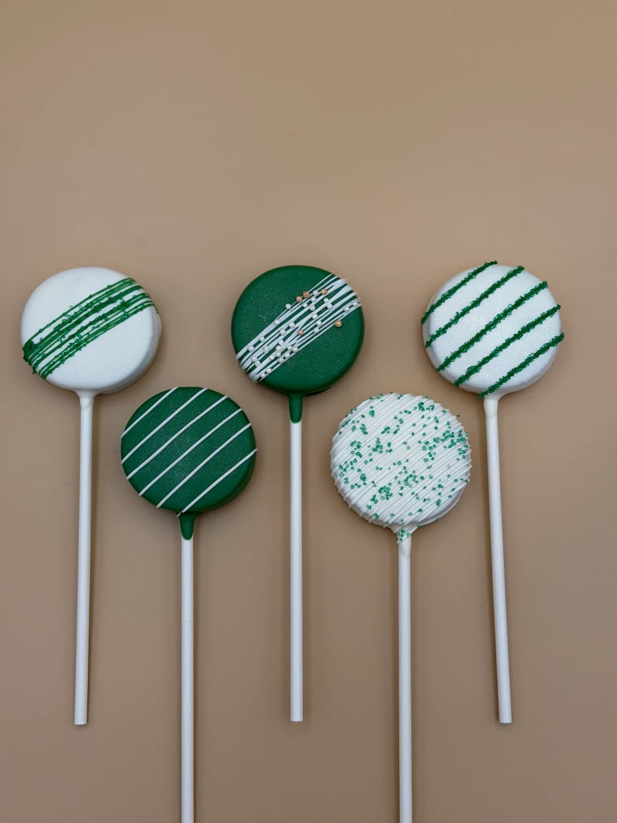 Five classic cake pops showing different green drizzle and sprinkle finishes