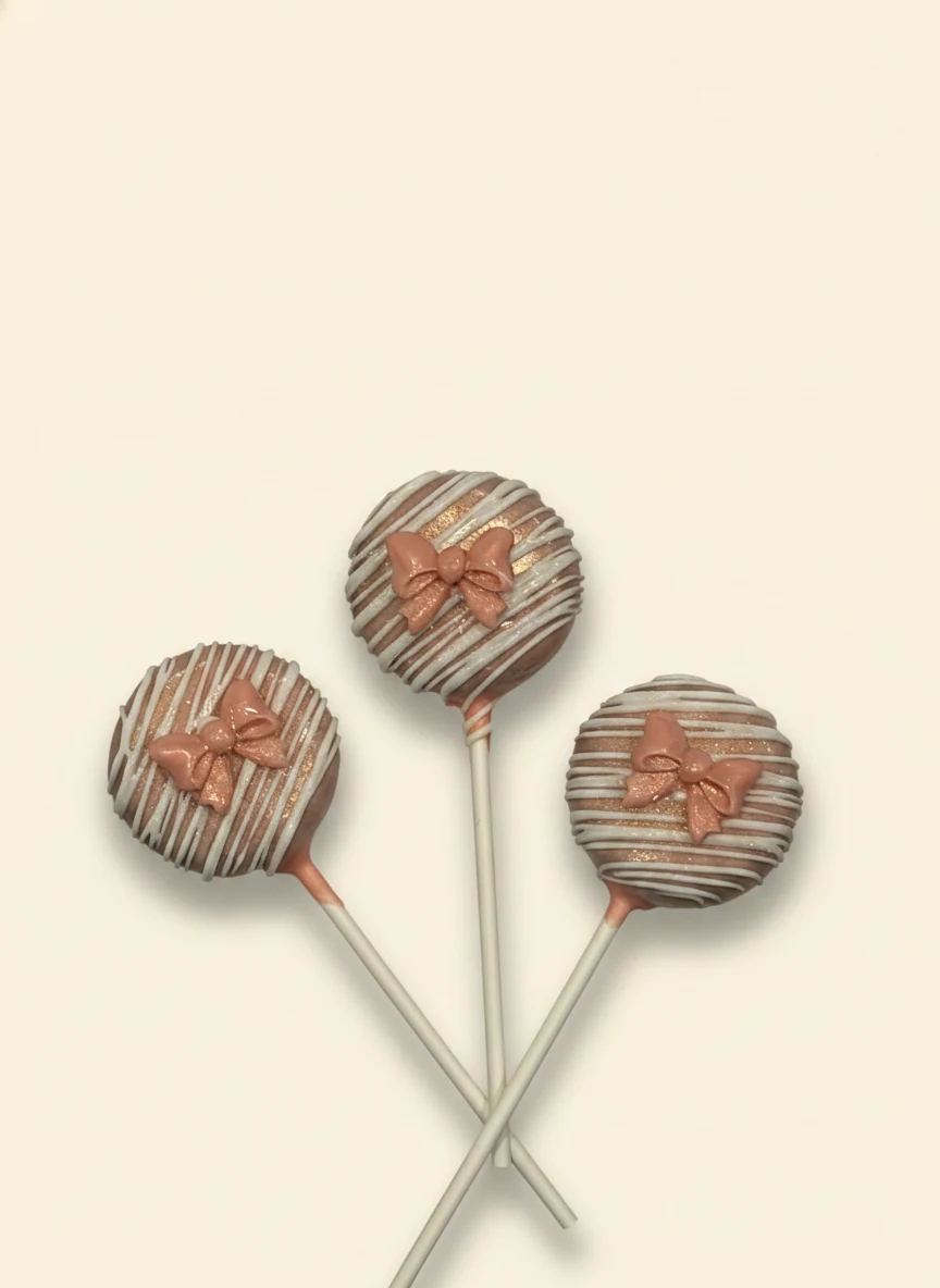 Round cake pops with rose-gold drizzle and small bow accents.