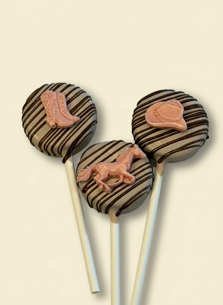 Cake pops with chocolate horse, cowboy boot, and cowboy hat decor on chocolate drizzle.